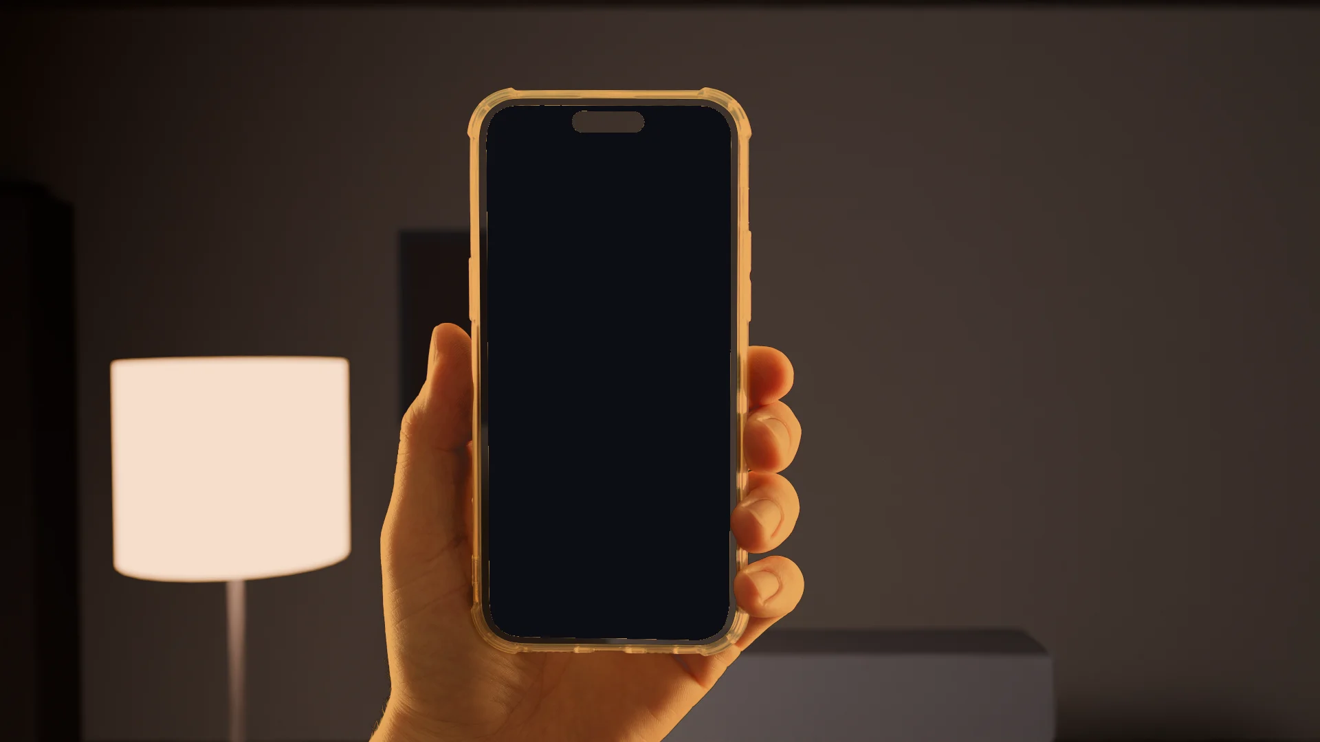 Une main tient un téléphone dans une pièce éclairée par une lampe, la nuit.